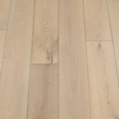 A photograph of a sand-coloured plank flooring. The planks feature a light, sandy hue with natural wood grain patterns, providing a warm and inviting appearance.